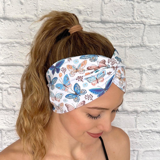 Woman with hair in ponytail wearing wide, twisted headband in white with butterfly print.