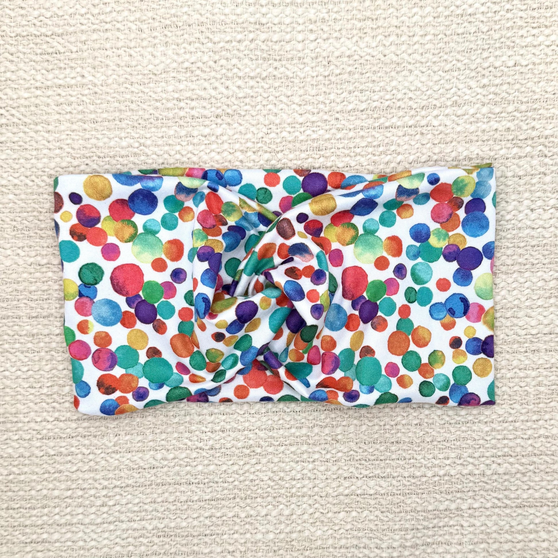 Wide, twisted headband in white with rainbow color polka dot print.