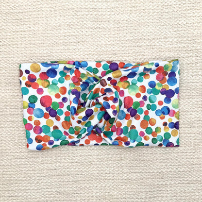 Wide, twisted headband in white with rainbow color polka dot print.