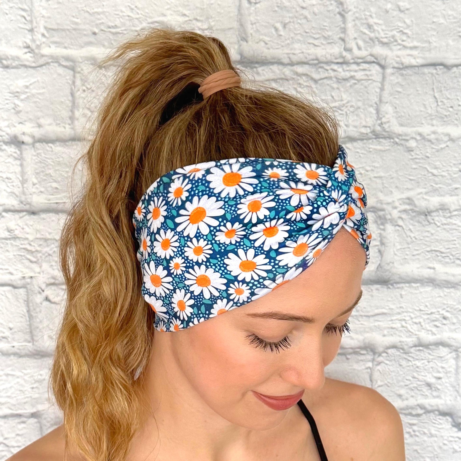 Woman with hair in ponytail wearing wide, twisted headband in blue with white daisy print.