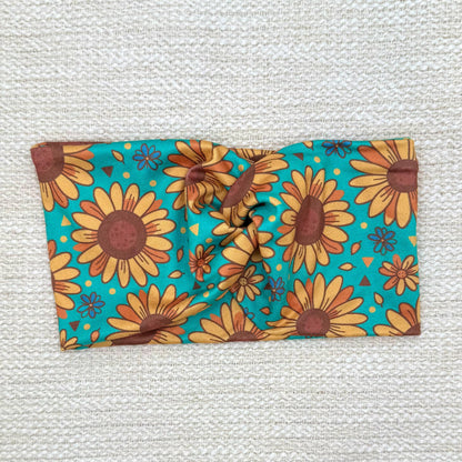 Wide, twisted headband in teal color with sunflower print.
