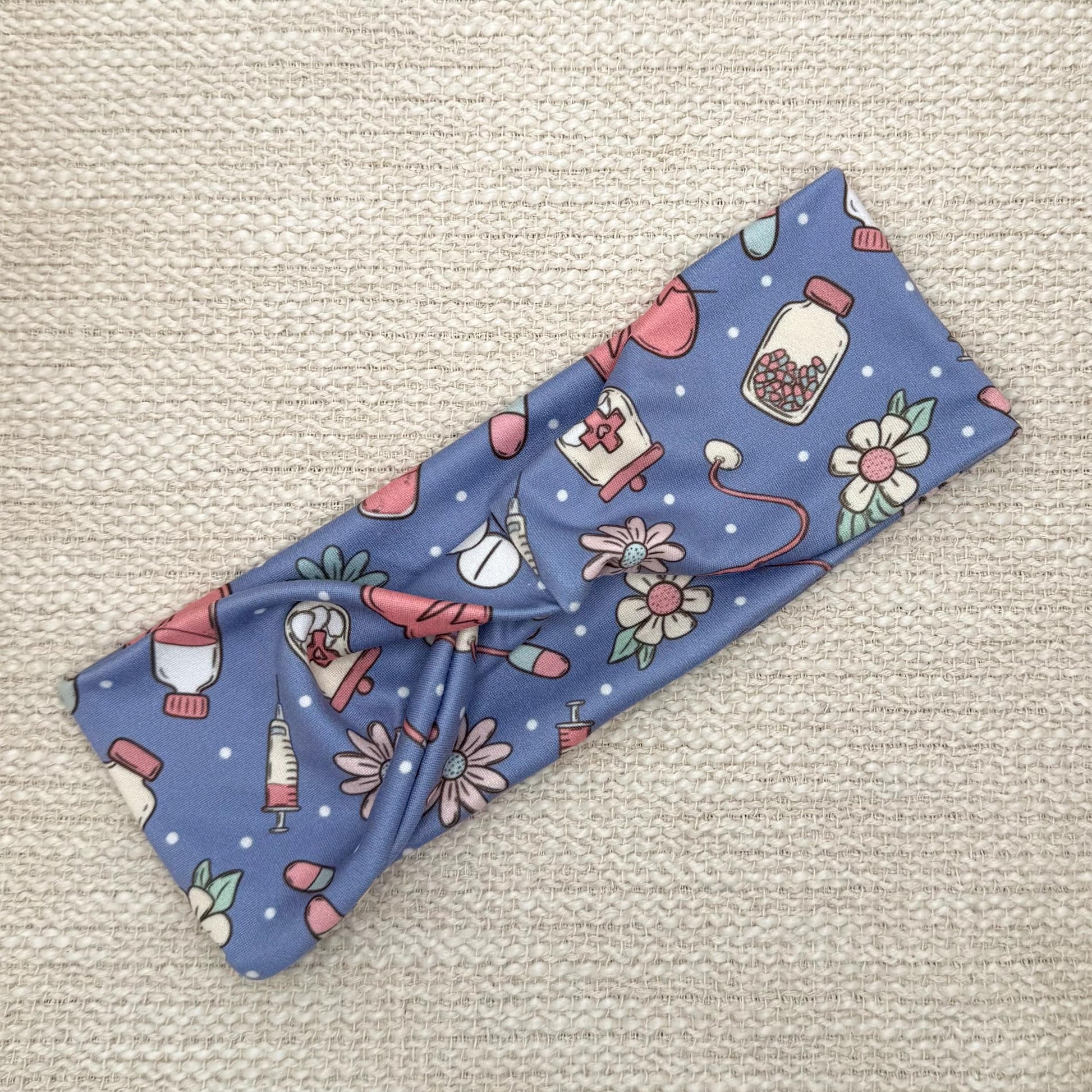 Flat, stretchy headband in blue with pink, white, and mint color medical theme print.