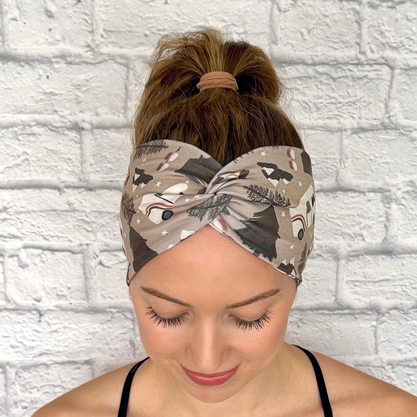 Woman with hair in ponytail wearing wide, twisted headband in tan with camping theme print.