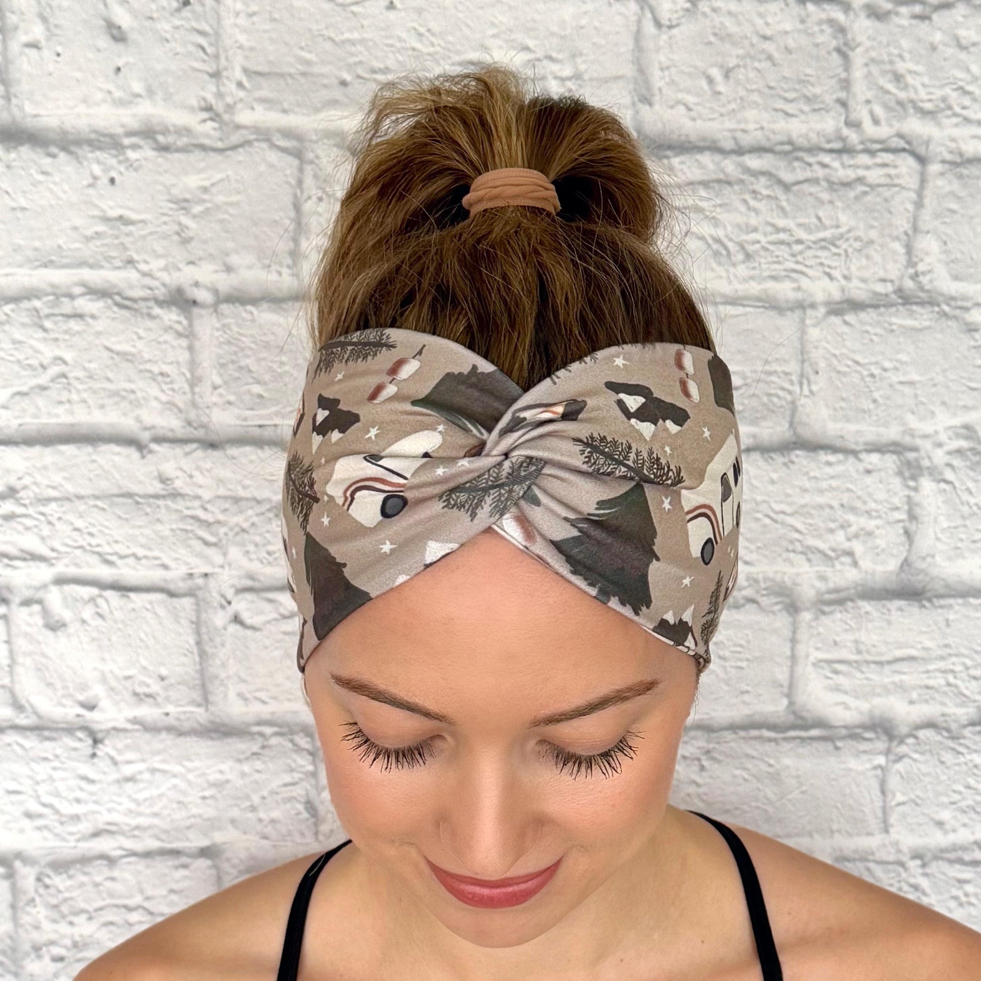 Woman with hair in ponytail wearing wide, twisted headband in tan with camping theme print.
