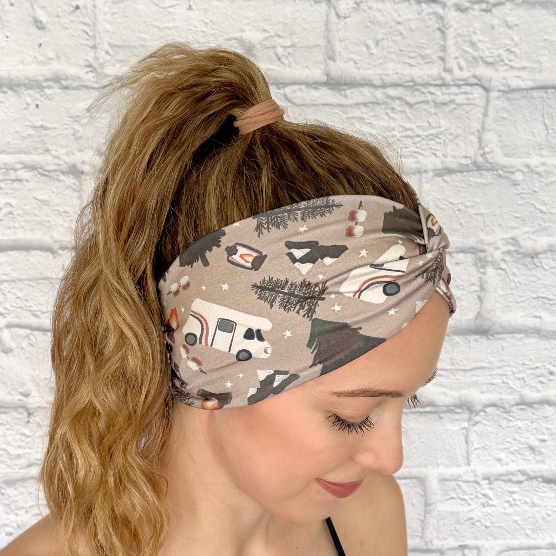 Woman with hair in ponytail wearing wide, twisted headband in tan with camping theme print.