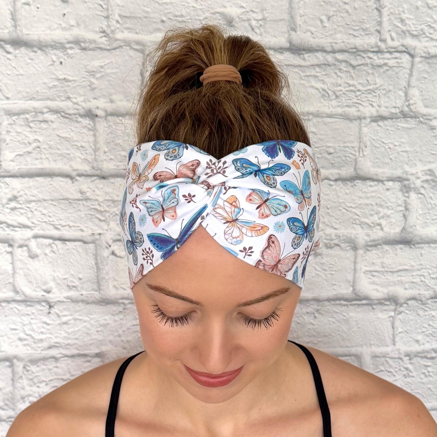 Woman with hair in ponytail wearing wide, twisted headband in white with butterfly print.