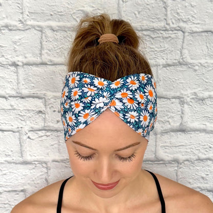 Woman with hair in ponytail wearing wide, twisted headband in blue with white daisy print.