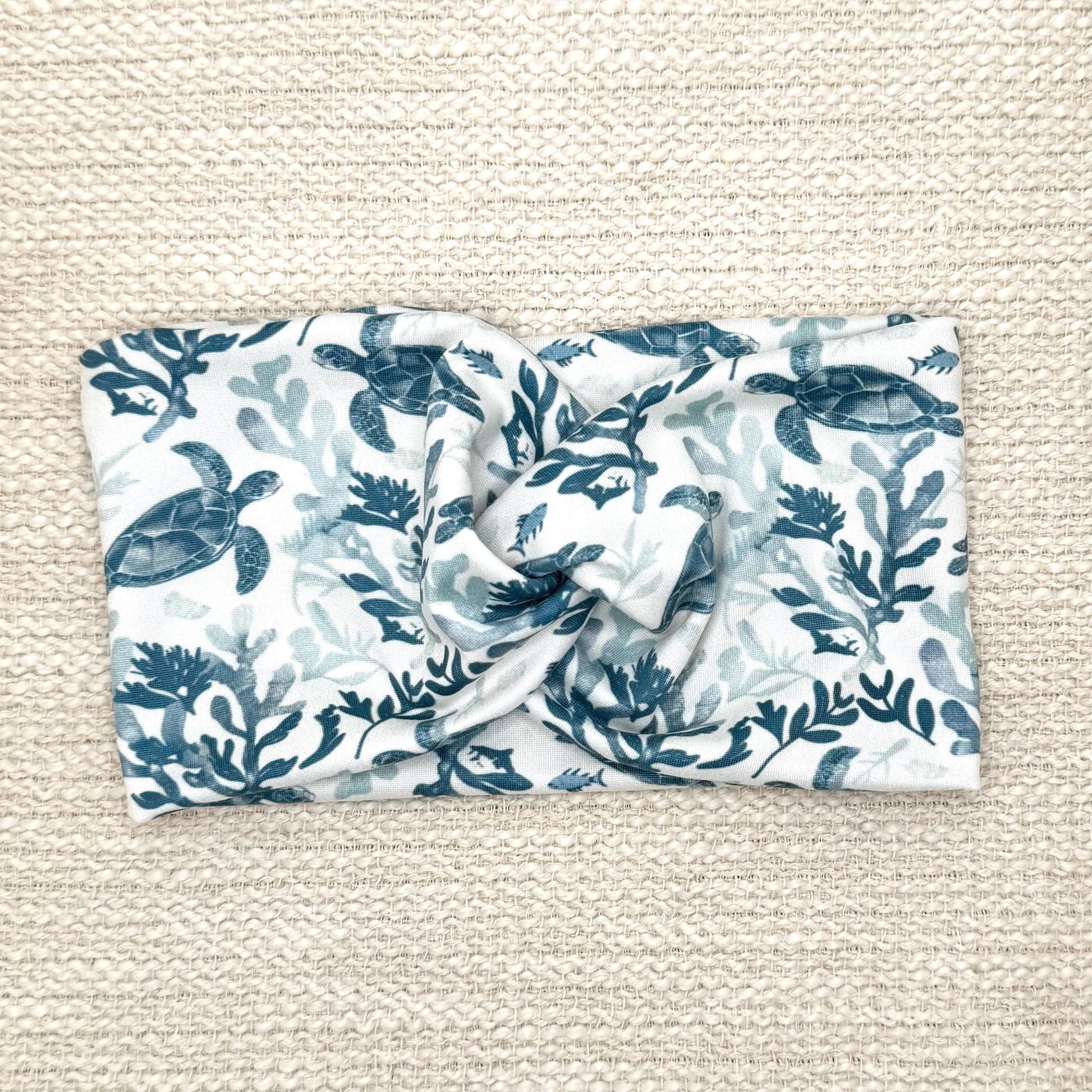 Wide, twisted, white headband with sea turtle print, displayed on cream background.