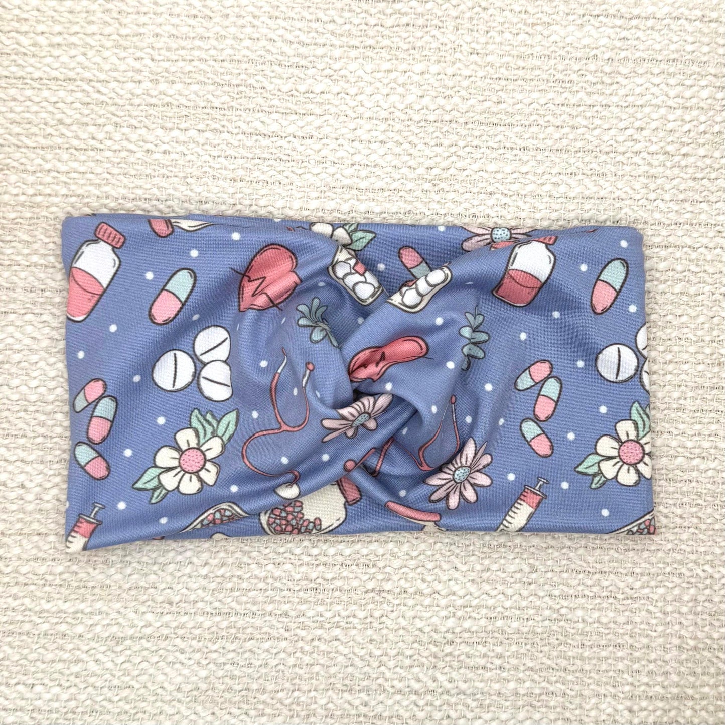 Wide, twisted headband in blue with pink, white, and mint color medical theme print.