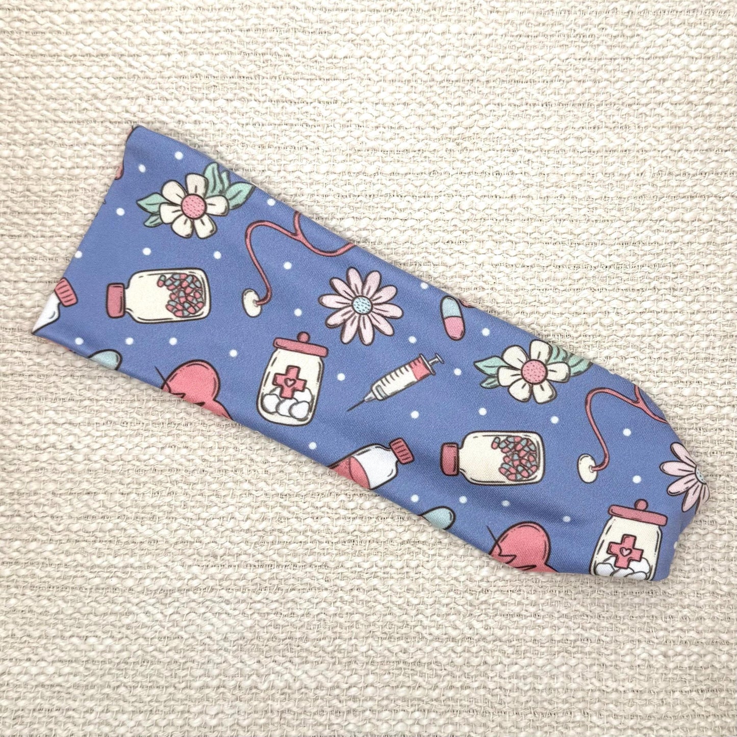 Flat, stretchy headband in blue with pink, white, and mint color medical theme print.