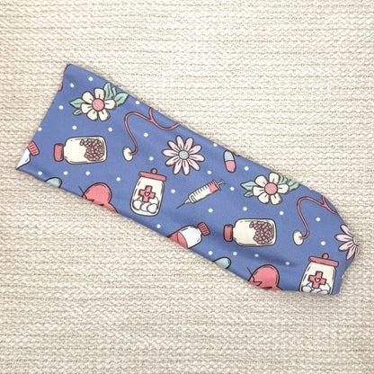 Flat, stretchy headband in blue with pink, white, and mint color medical theme print.