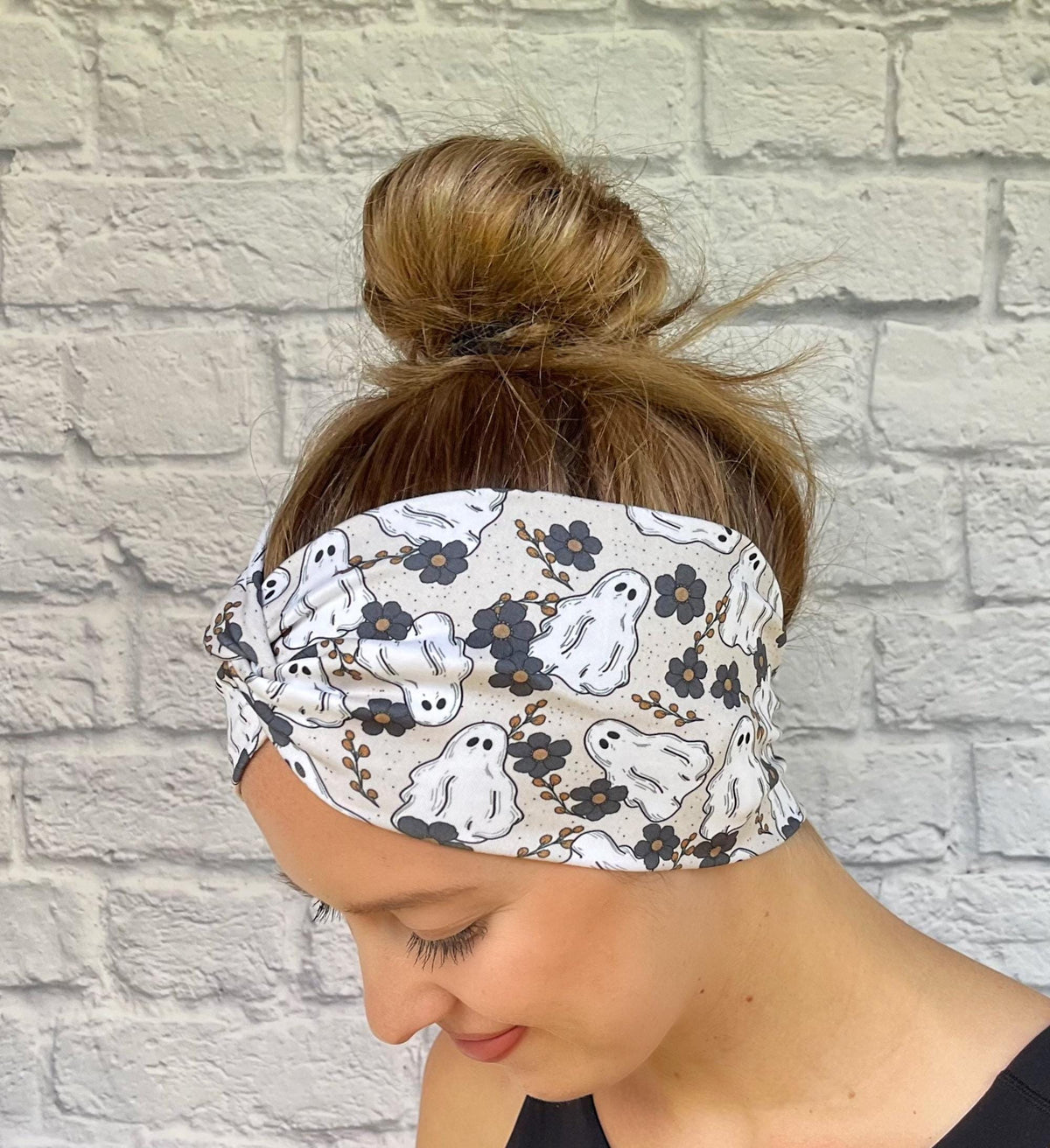 Woman with hair in bun wearing wide, twisted headband in cream/gray with floral and ghost print.