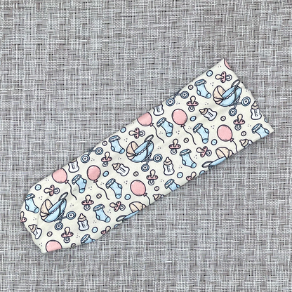 cream headband with baby theme print- baby bottles, socks, balloons, binkies, and buggy