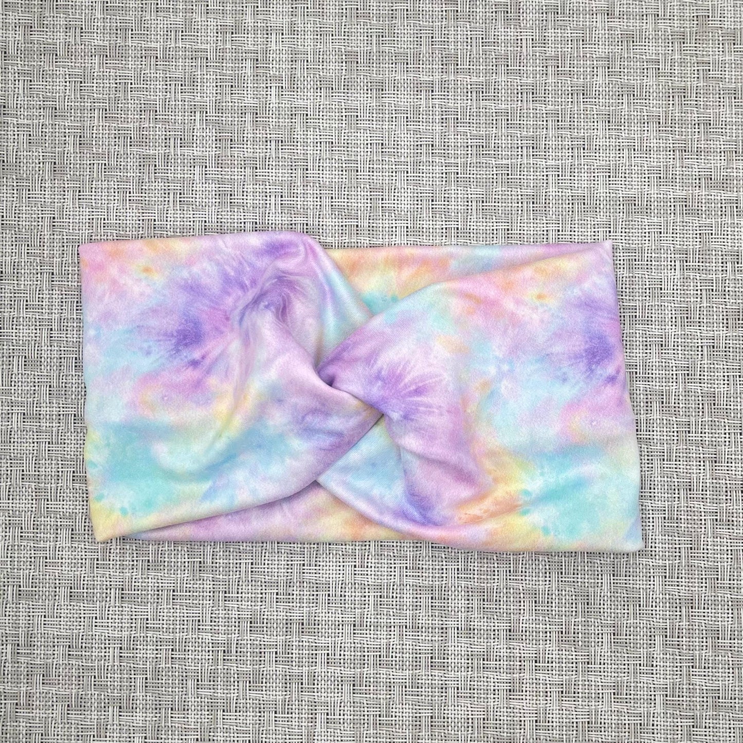 Wide, twisted headband with pastel color tie dye print on gray background.