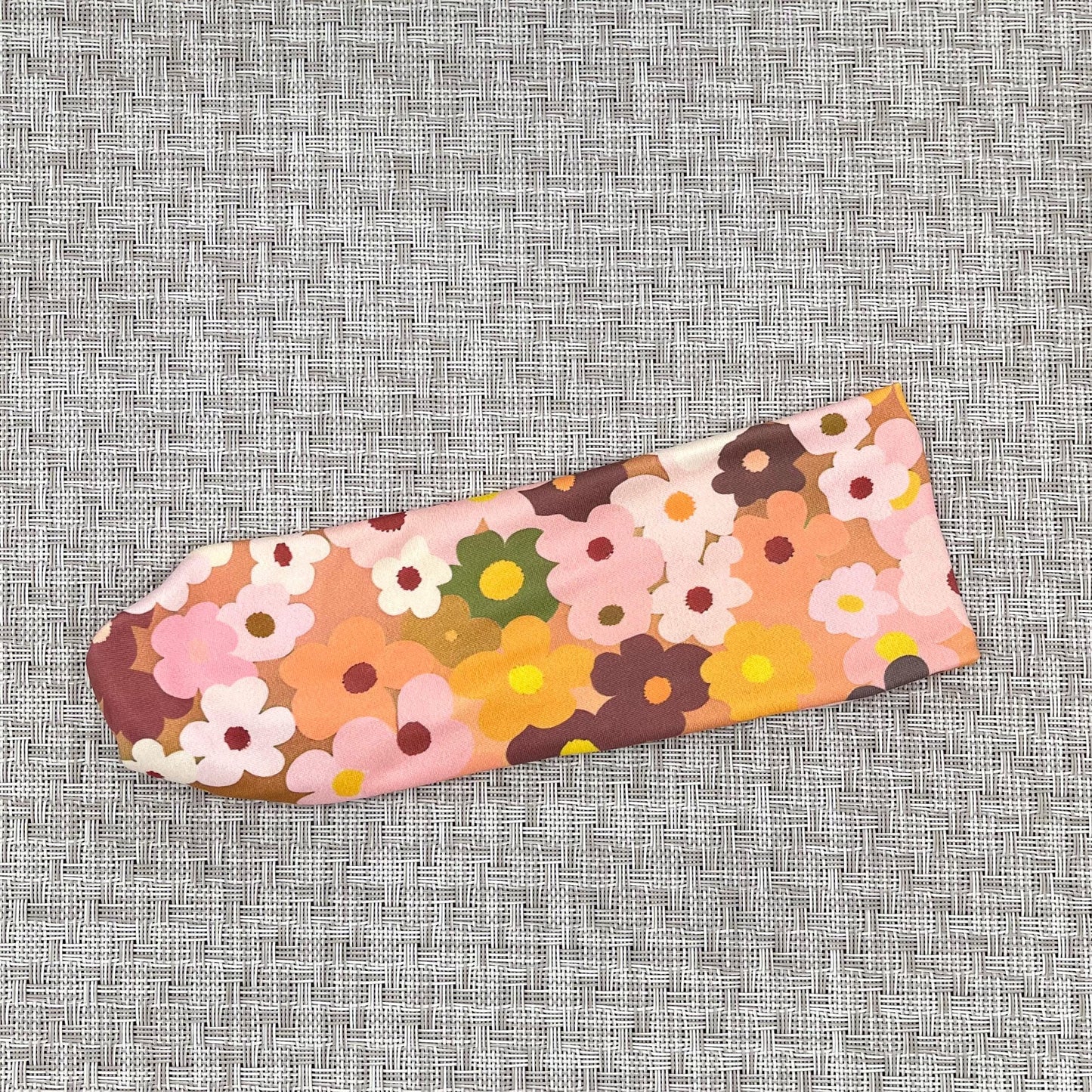 Flat headband in peach color with light and dark pink, navy, white, yellow, and orange flower print.