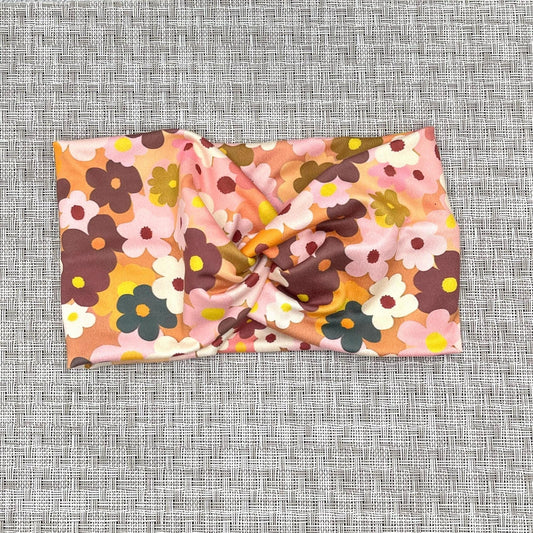 Wide, twisted headband in peach color with light and dark pink, navy, white, yellow, and orange flower print.