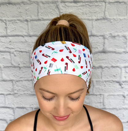 Woman with hair in ponytail wearing white headband with phlebotomy theme print- blood vials, blood drops, and syringes.