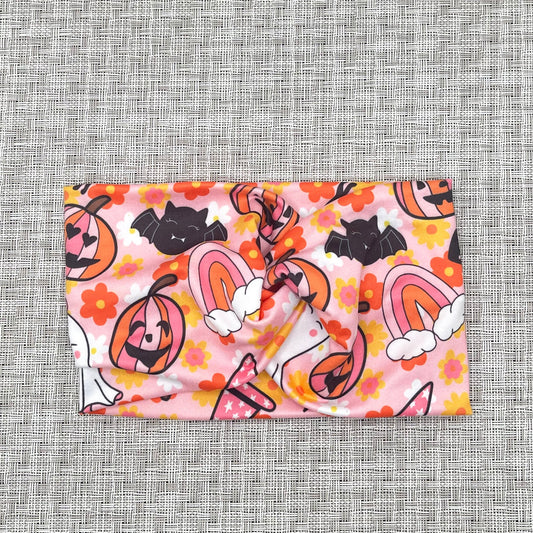 pink, wide twist headband with bats, rainbows, flowers, pumpkins, and ghosts with pink, orange, yellow, and white color theme