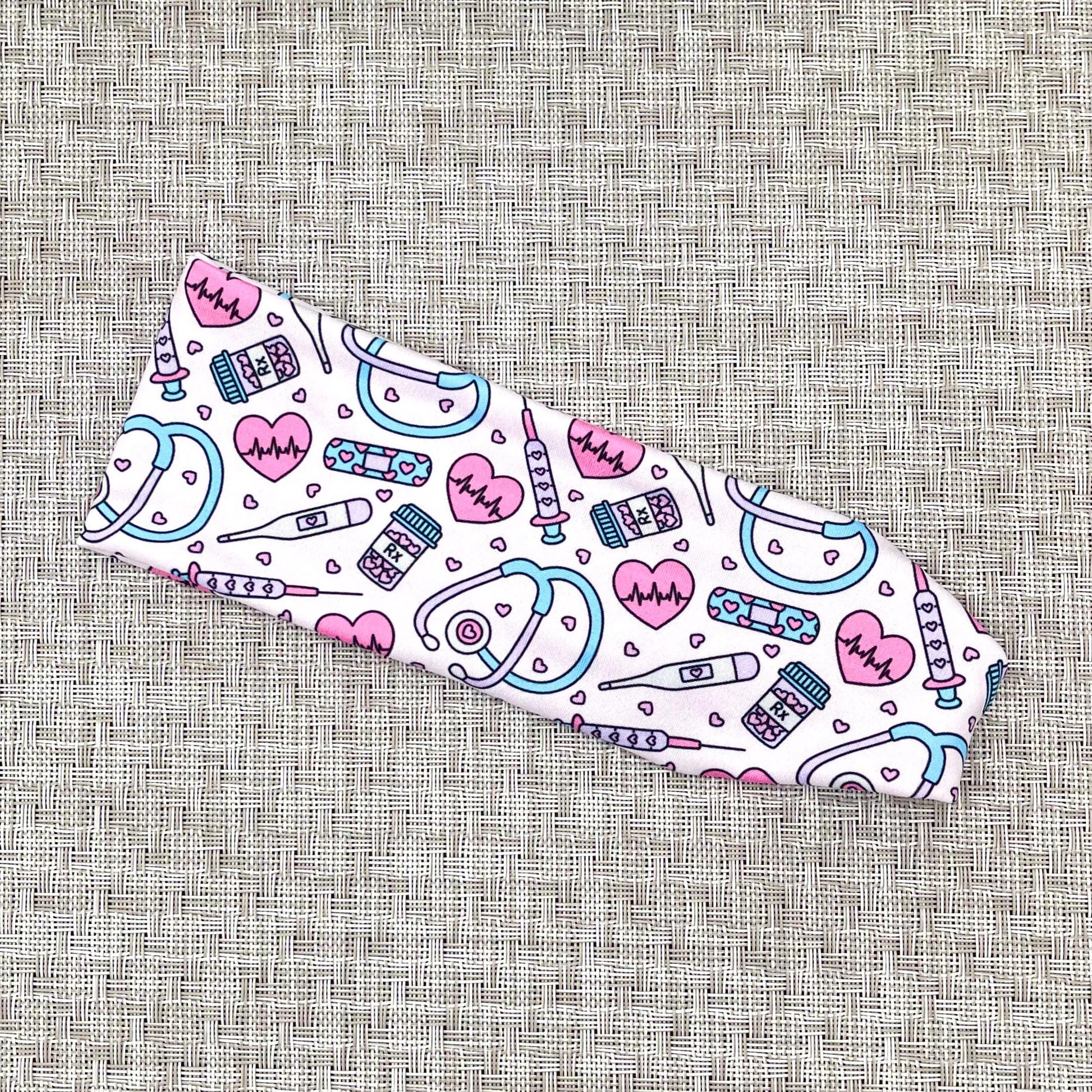 Flat, stretchy headband in light pink with pink, purple, and blue medical theme print.