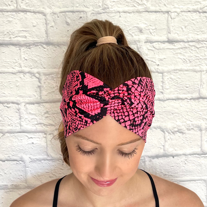 Woman with hair in curled ponytail wearing wide, twisted headband in hot pink with black snakeskin print.