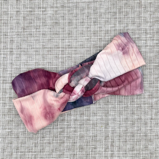 Pink tie dye knotted headband in ribbed fabric on gray background.