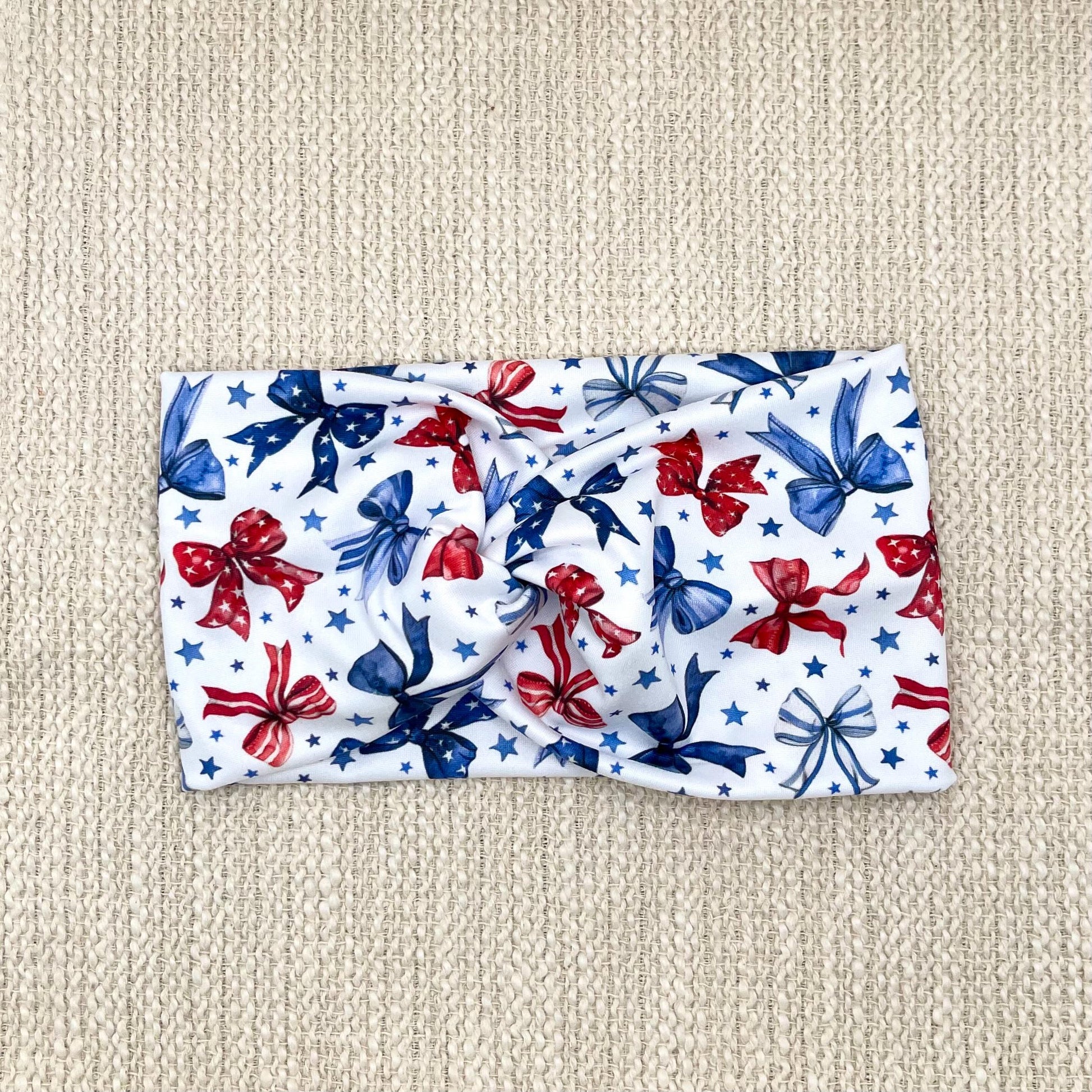 Wide, twisted, white headband with red and blue bows and blue star print.