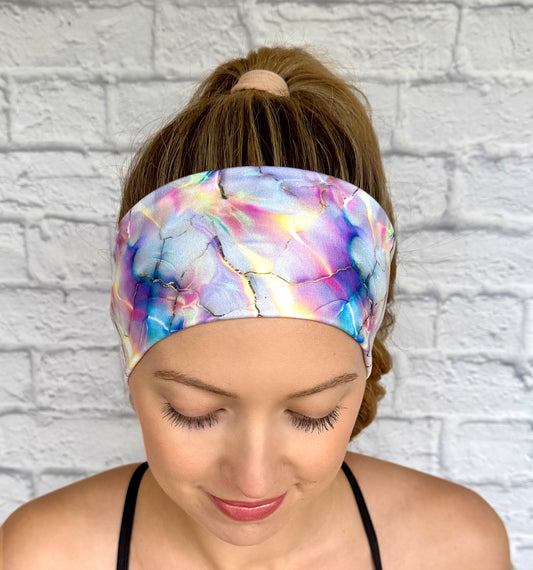 Woman with hair in ponytail wearing flat, stretchy headband in multicolor watercolor print.