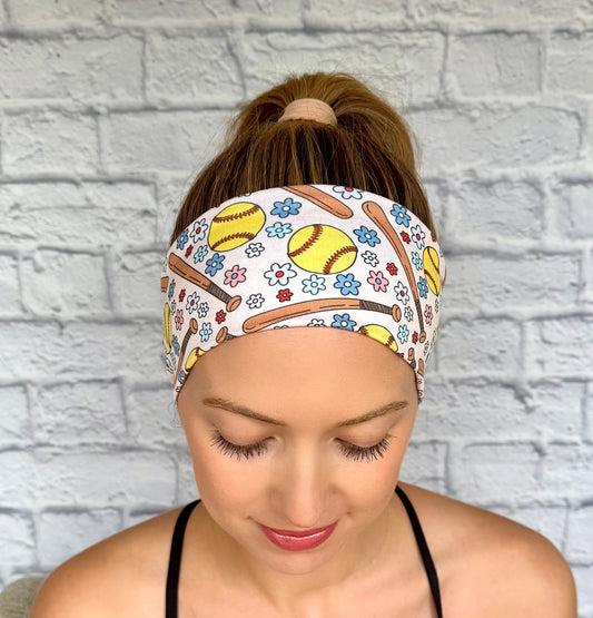 Woman with hair in ponytail wearing flat, stretchy headband in cream color with softball and flower theme print.