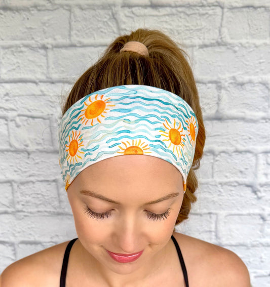 Woman with hair in ponytail wearing flat, stretchy headband with blue waves and sun print.