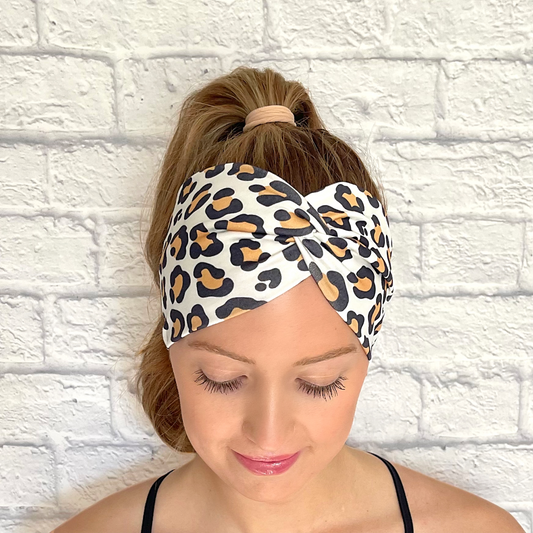 Woman with hair in ponytail wearing wearing wide, twisted headband in white with tan and black cheetah print.