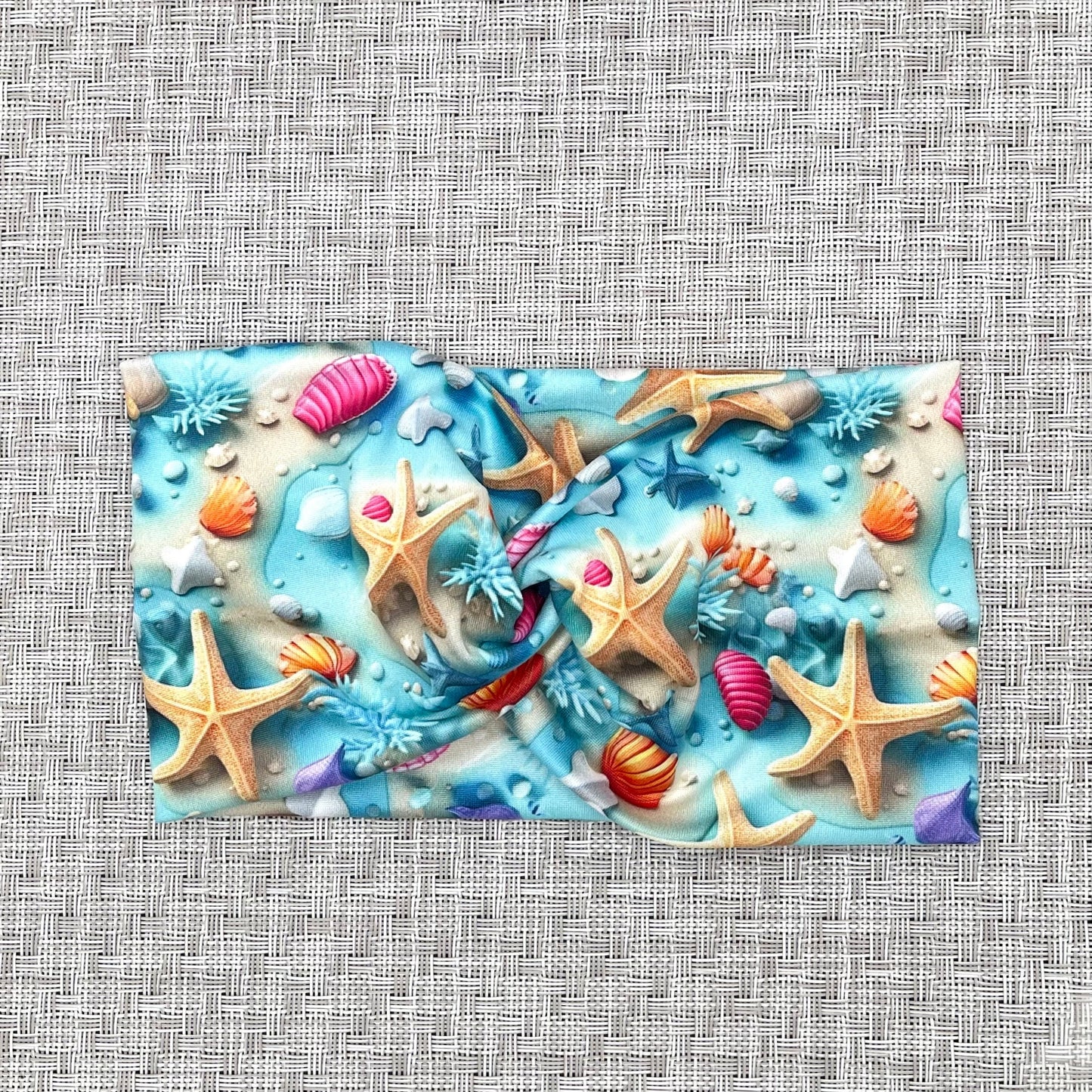 light blue wide twist headband with ocean theme print- water, sand, starfish, and shells