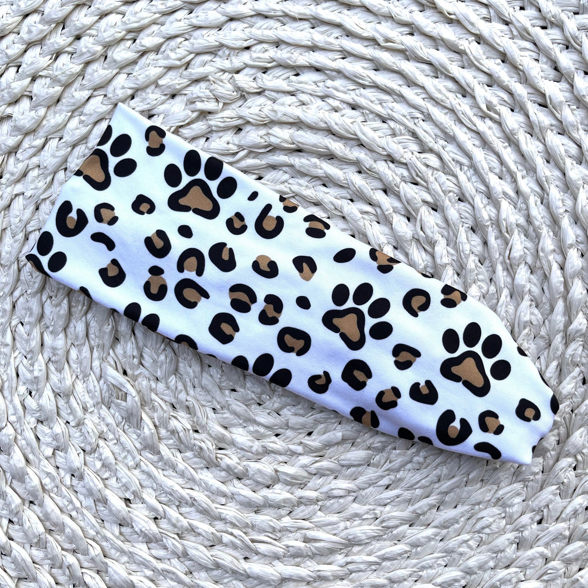 Flat, stretchy, white headband with dog paw and cheetah print in brown and black.