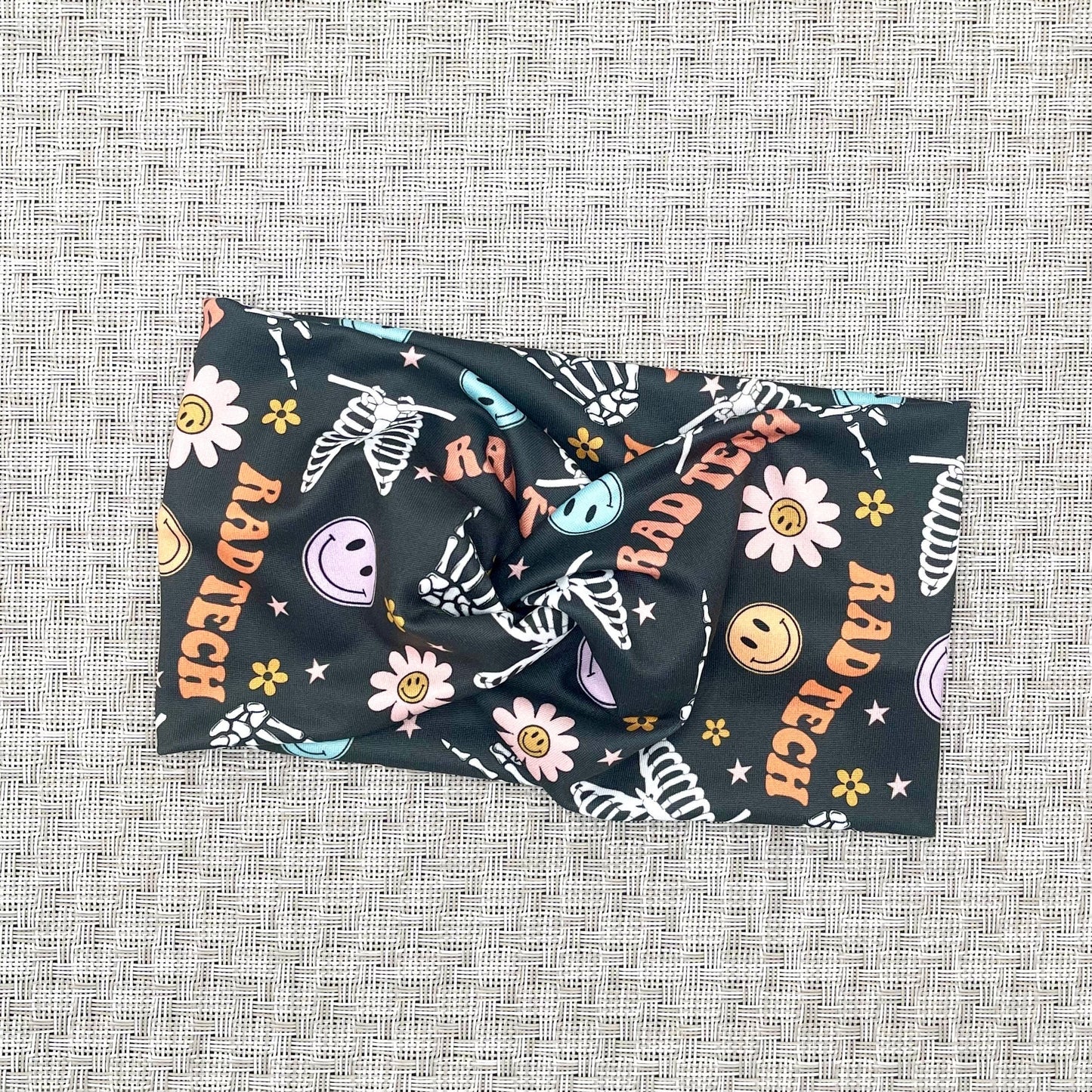 gray headband with "rad tech", smiley faces, flowers, and skeletons